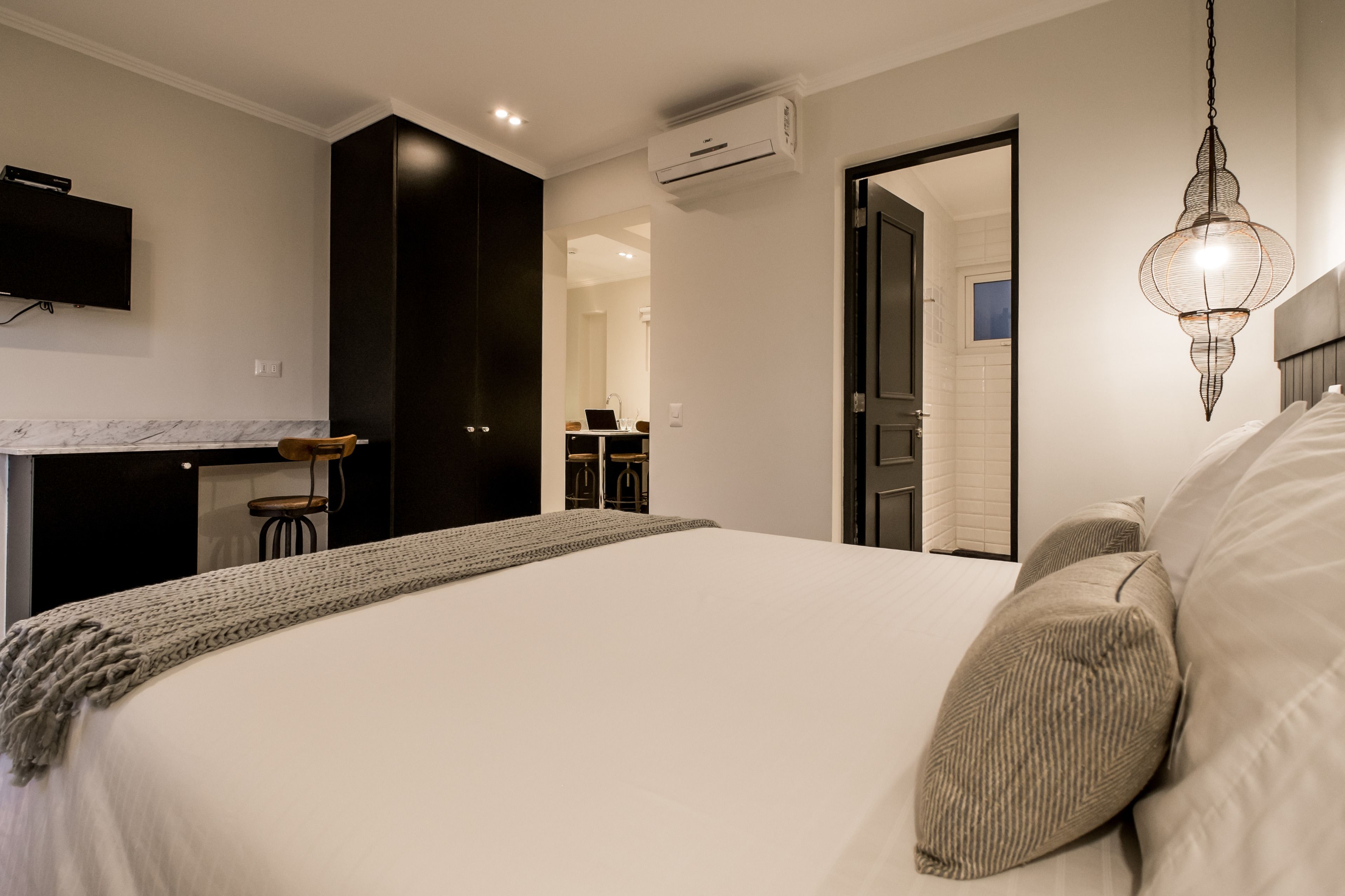A bedroom with a large bed, a TV mounted on the wall, and an air conditioning unit.