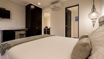 A bedroom with a large bed, a TV mounted on the wall, and an air conditioning unit.