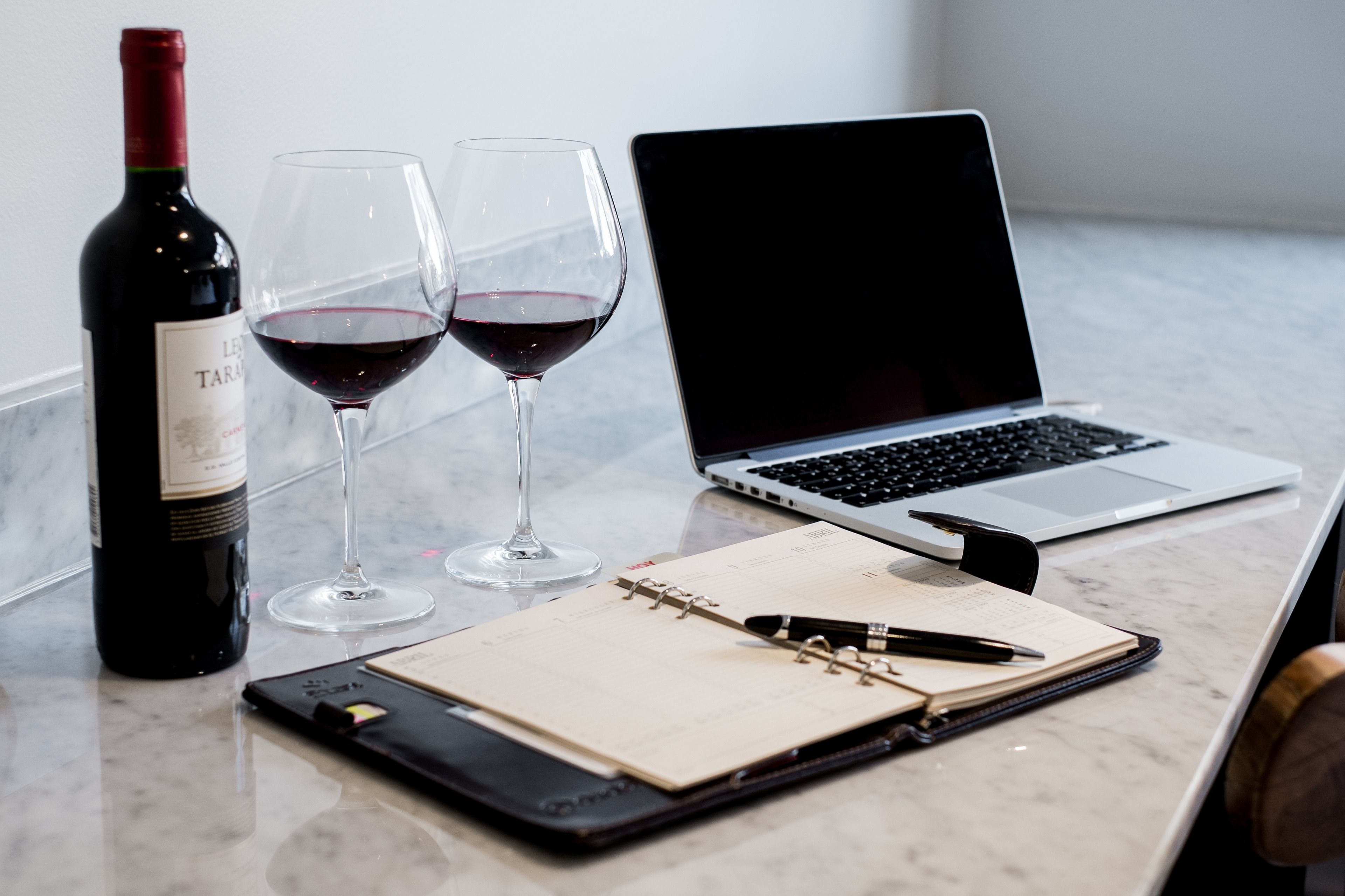Un ordenador portátil, una botella de vino y dos copas de vino sobre una mesa de mármol.