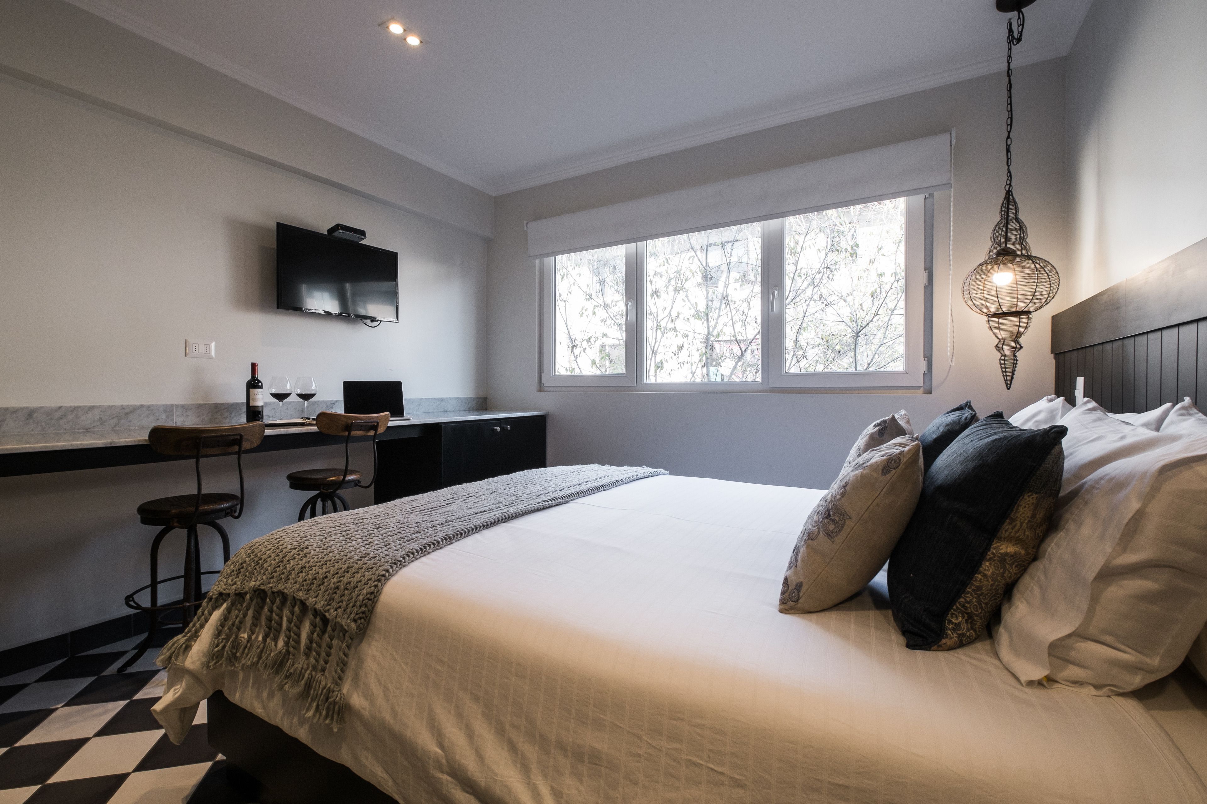 A bedroom with a bed, a TV mounted on the wall, a window, and a desk with two chairs.