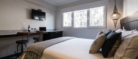 A bedroom with a bed, a TV mounted on the wall, a window, and a desk with two chairs.