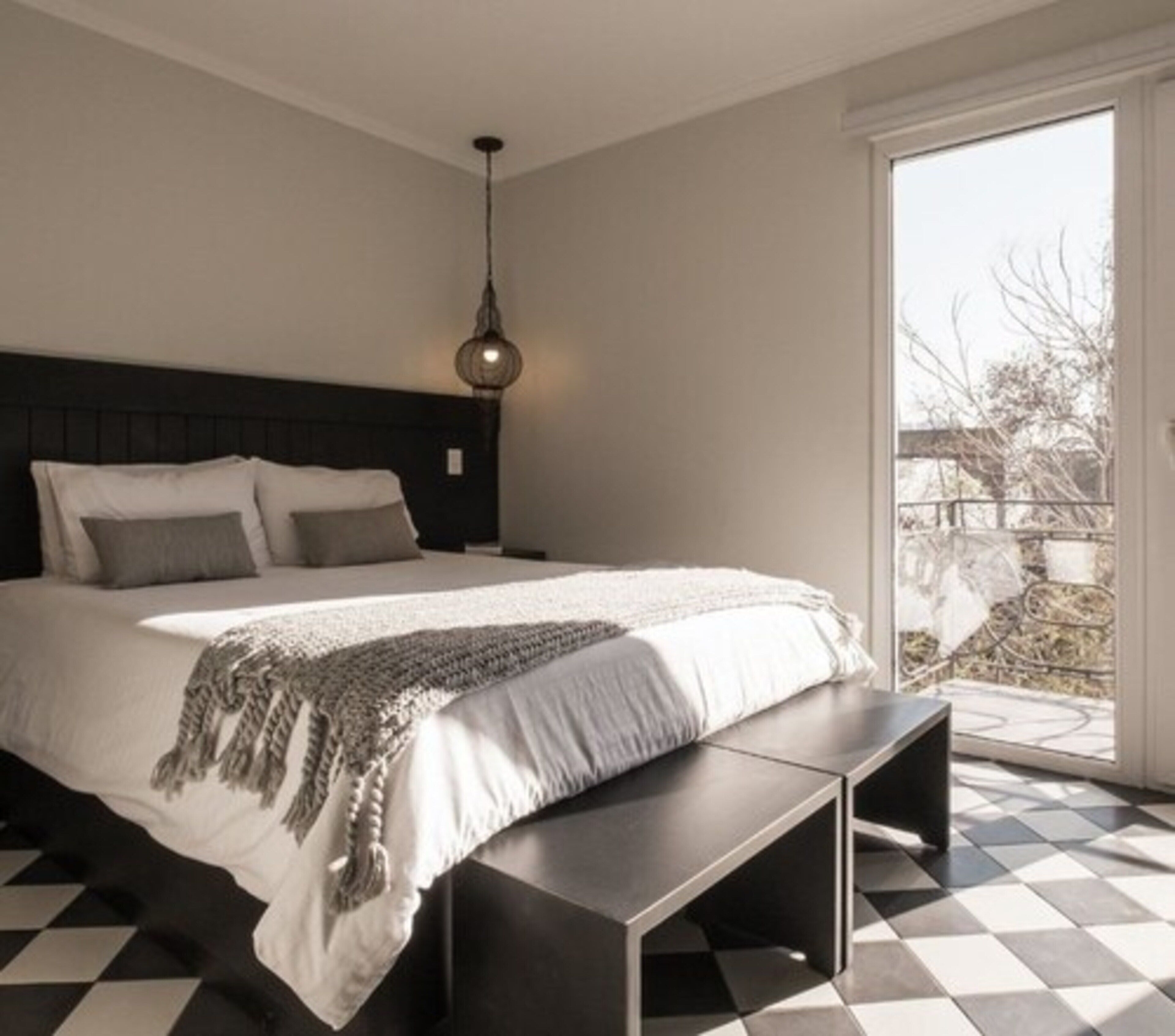 Een slaapkamer met een groot bed, een bankje, een hanglamp en uitzicht op het omliggende landschap door een groot raam.