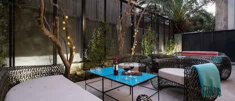 An outdoor seating area with wicker furniture and a blue table, surrounded by trees and a fence.