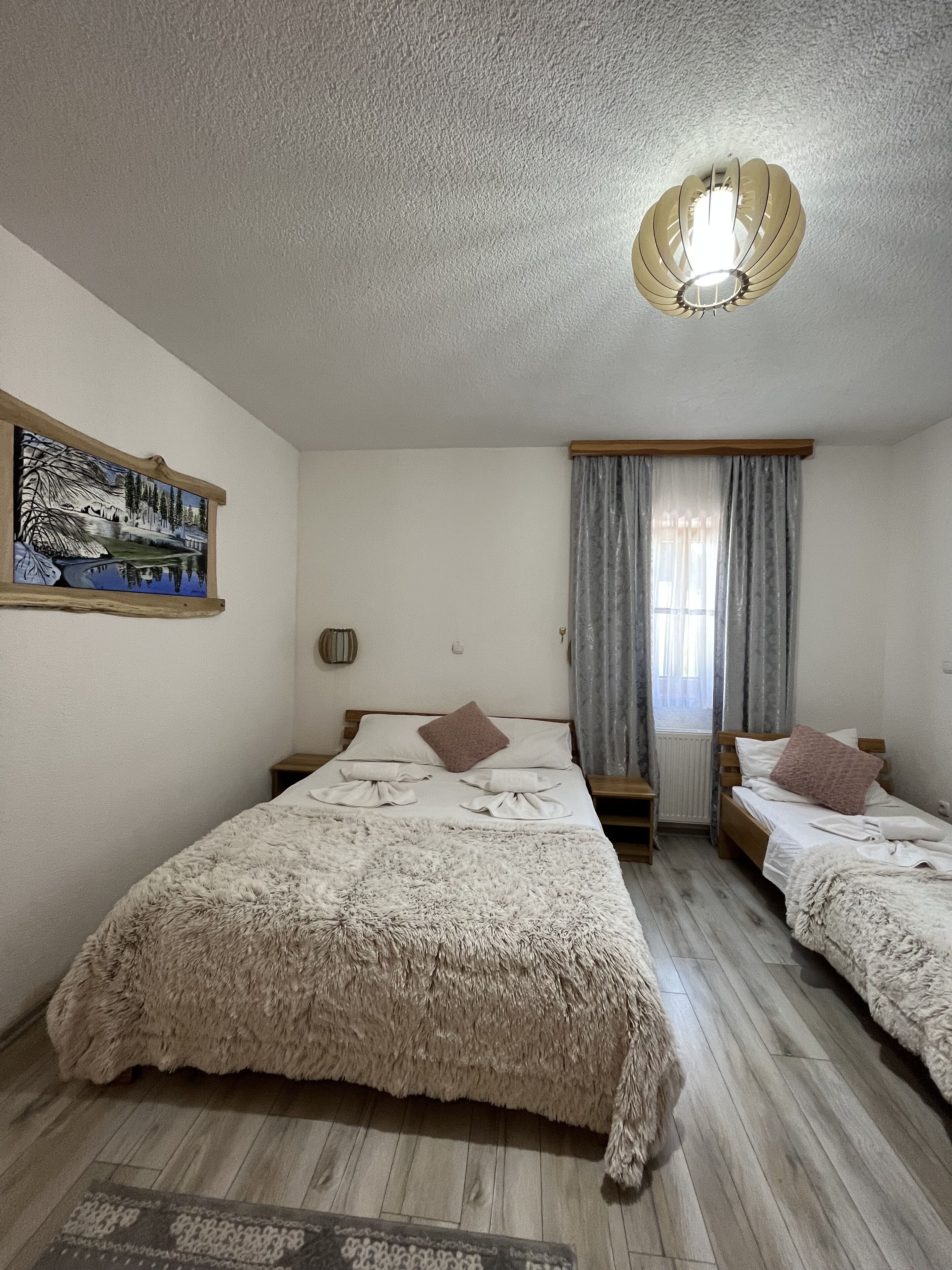 A bedroom with two beds, a ceiling fan, a painting, and a window with curtains.