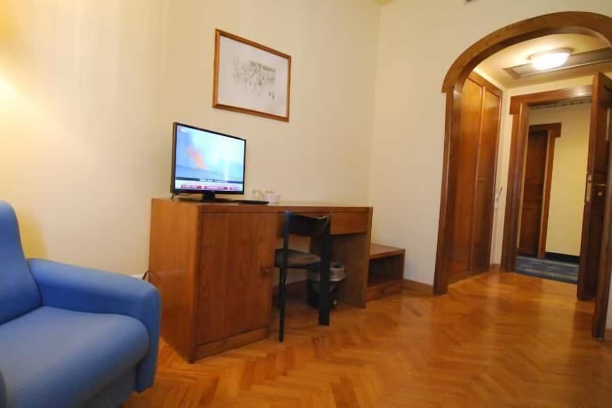 A room with a blue sofa, a wooden desk with a computer, and a framed picture on the wall.