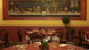 A restaurant with tables set for dining, a large painting on the wall, and a small plant on the table. - Hotel Moderno (Pontassieve)