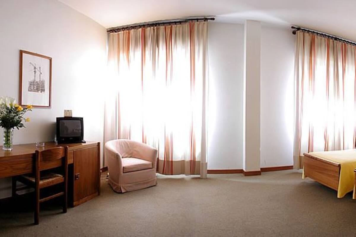 A hotel room with a bed, a desk, a chair, a television, and curtains.