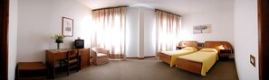 Hotellihuone, jossa on sänky, työpöytä, tuoli, televisio ja verhot.