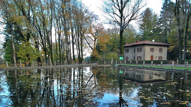 A calm lake reflecting trees and a building with a red roof. - Hotel Moderno (Pontassieve)