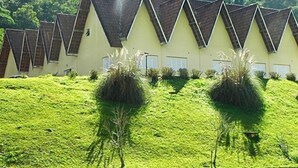 A row of triangular-roofed buildings with a green lawn in front. - Hotel H Santo Antonio do Pinhal (Monteiro Lobato)