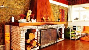 A stone fireplace with a wooden mantel, logs stored below, and a rustic stone wall. - Hotel H Santo Antonio do Pinhal (Monteiro Lobato)