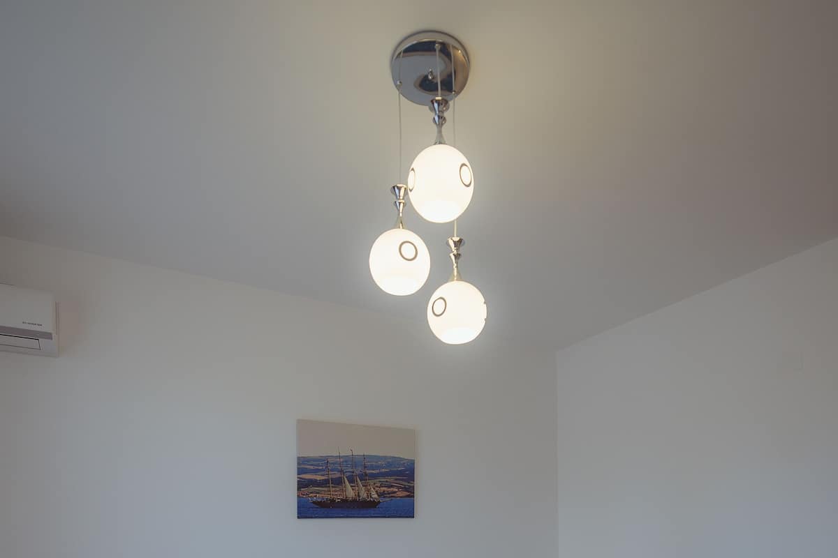 A bedroom with a bed, bedside lamps, a ceiling light fixture, and a wall-mounted painting.