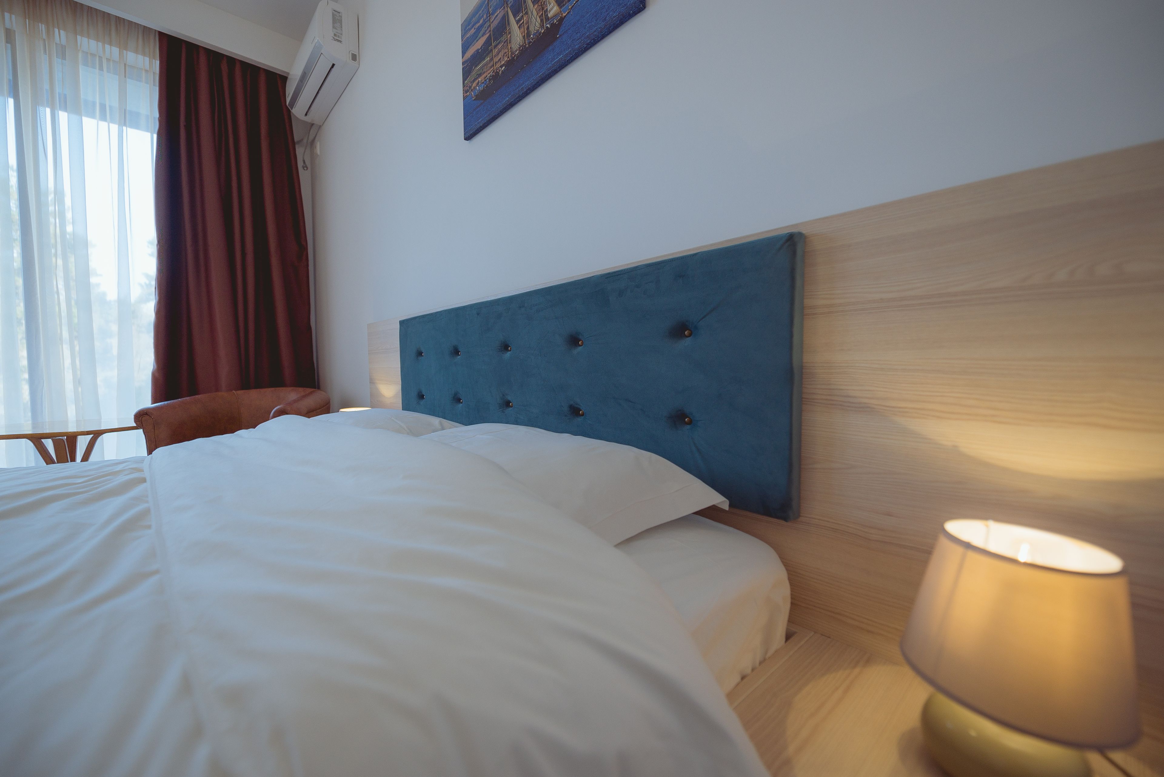A neatly made bed with white linens, a blue headboard, and a bedside lamp.