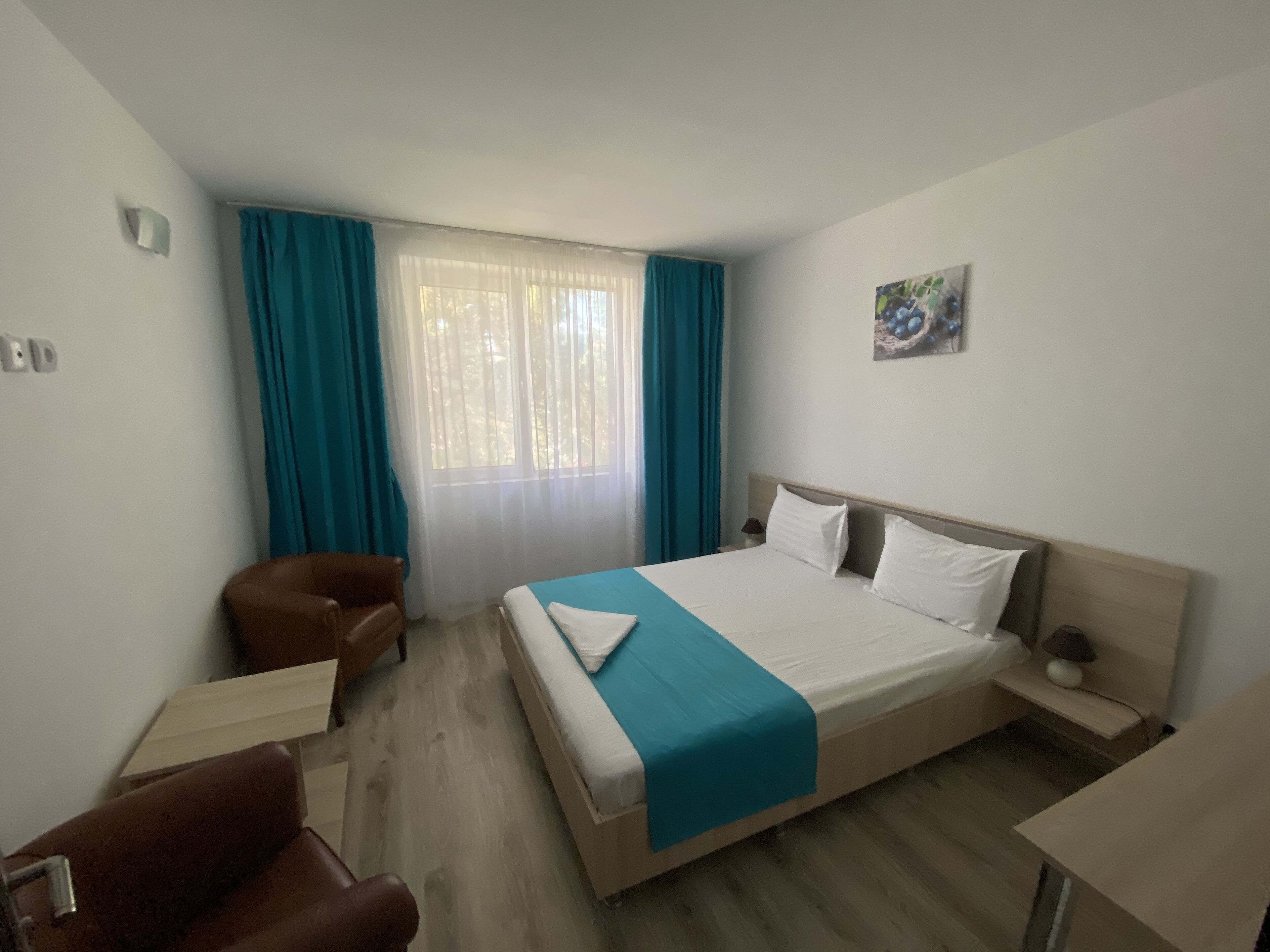 A hotel room with a bed, a chair, a desk, and a window with curtains.