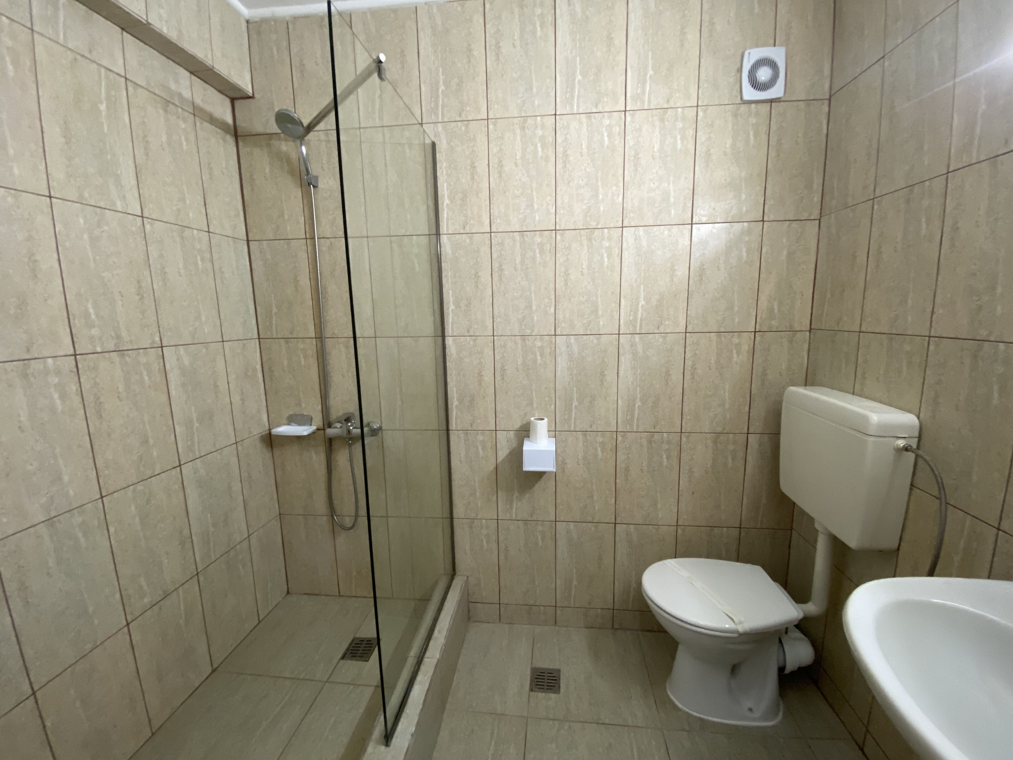 A bathroom with a glass-enclosed shower, a toilet, and a sink.