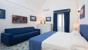 Una habitación de hotel con una cama, un sofá azul, un armario blanco y una ventana con cortinas azules.
