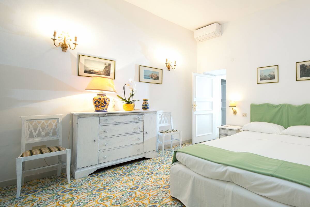 Un dormitorio con cama, cómoda, silla y lámparas fijadas en la pared.