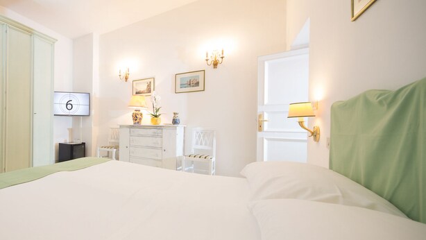 Una habitación de hotel con una cama grande, un aparador, un escritorio con silla, un televisor y lámparas fijadas a la pared.