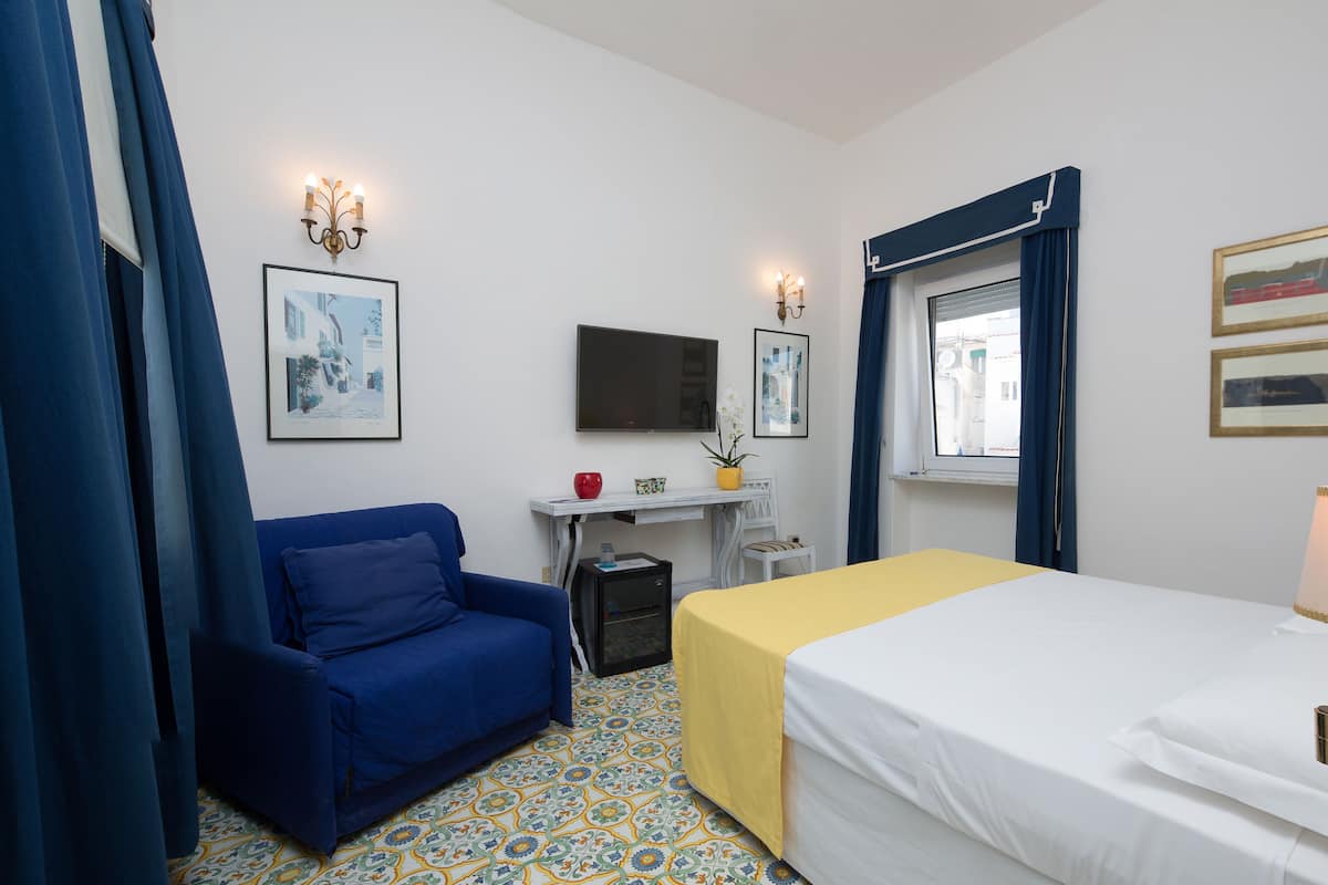 Habitación de hotel con cama, escritorio, silla, televisión y ventana con cortinas.