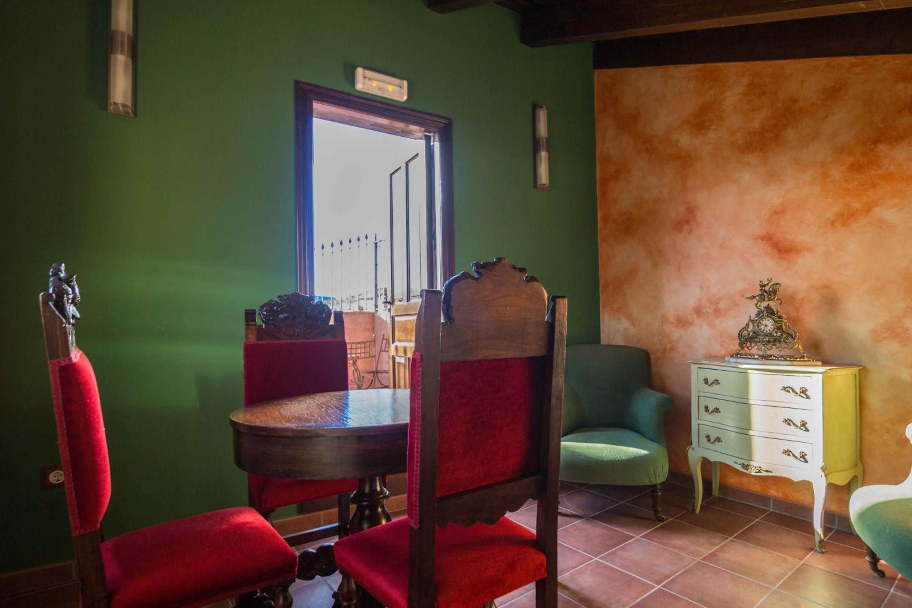 Un comedor con una mesa y sillas de madera, una pared verde y vistas a través de una ventana.