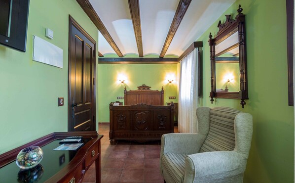 Una habitación con una cama de madera, una silla, un escritorio con un cuenco de vidrio y un espejo en la pared.
