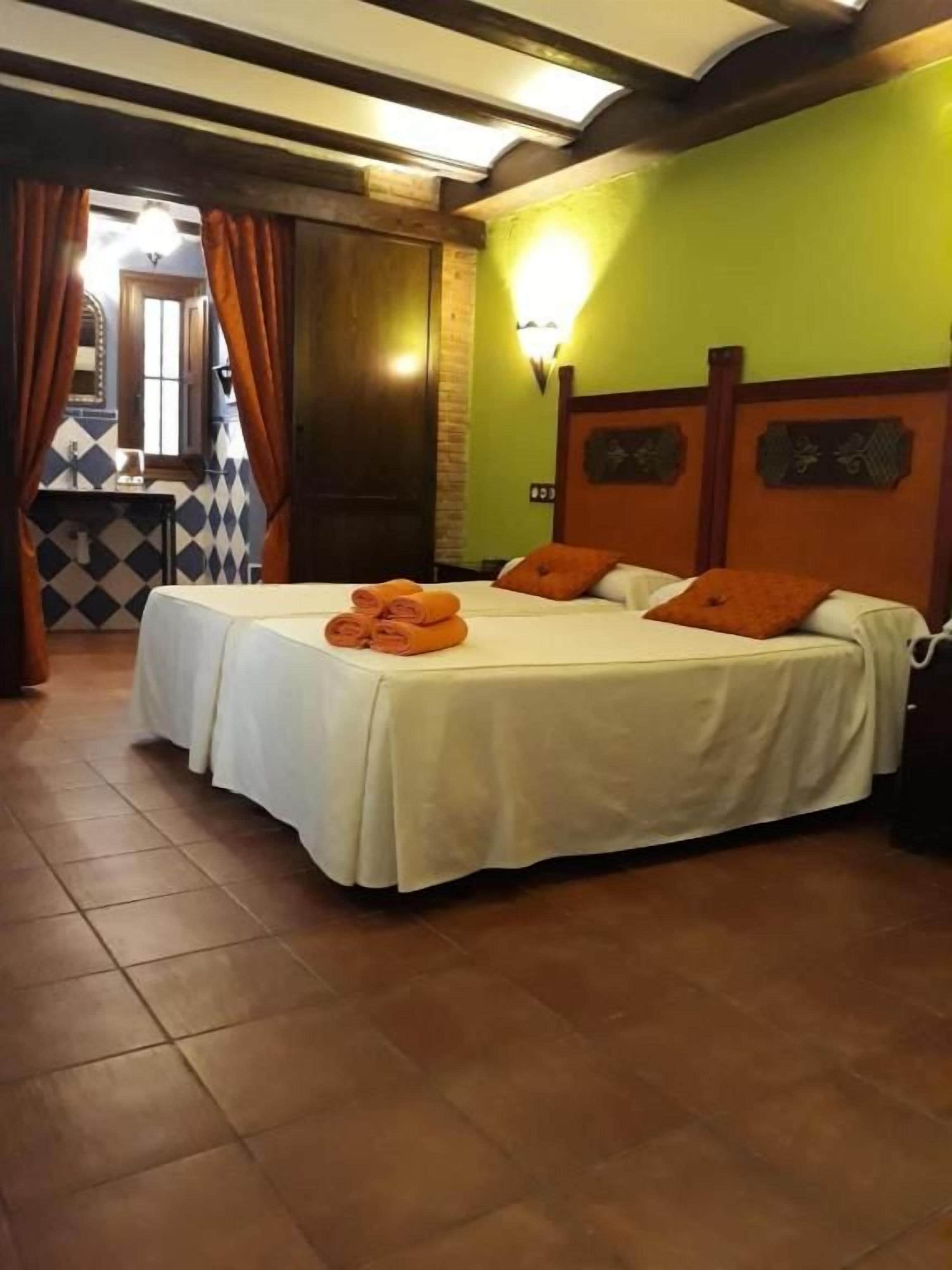Una habitación de hotel con dos camas, un cabecero de madera, una lámpara de pared y suelo de baldosas.