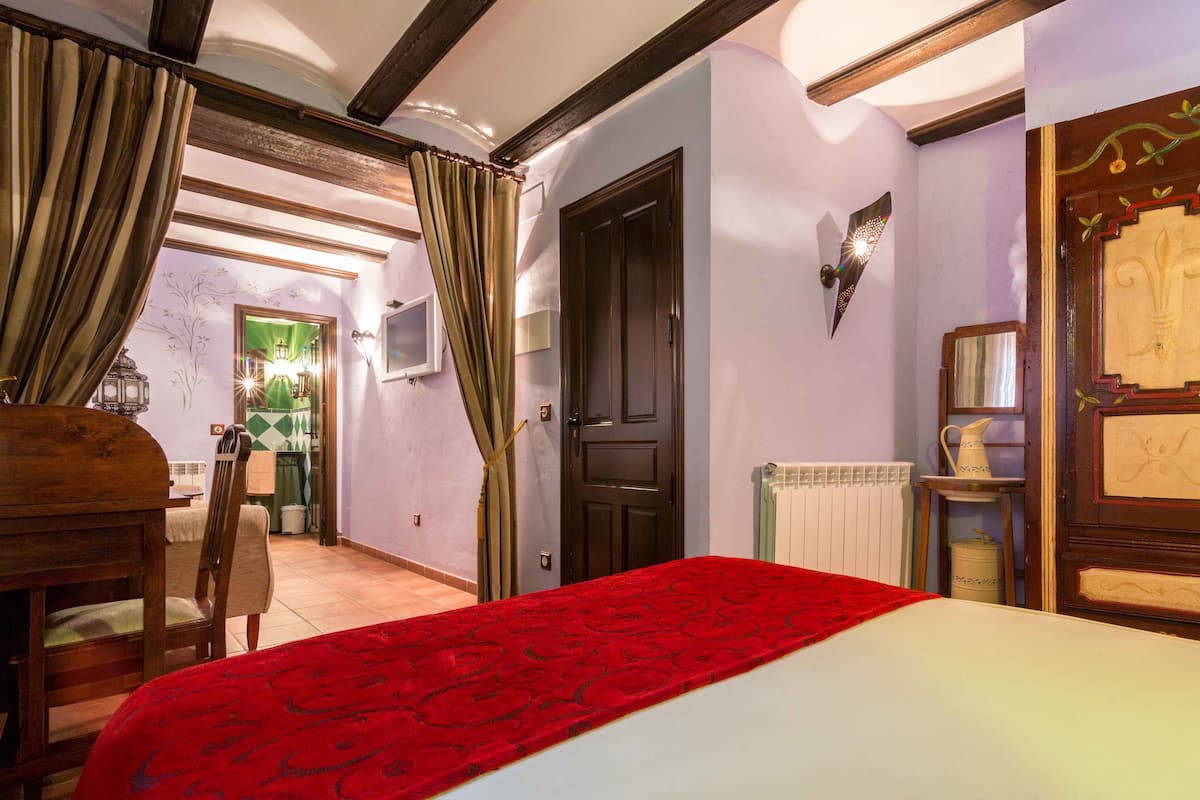 Une chambre d’hôtel comprenant un lit, une commode en bois, une chaise, un radiateur et une porte ornée de panneaux décoratifs.