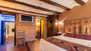 Un dormitorio con una cama grande, una silla de madera, un televisor montado en la pared y un cabecero estampado.