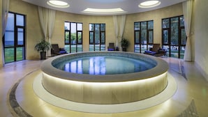 A luxurious indoor swimming pool with a skylight ceiling, large windows, and a view of the outdoors.