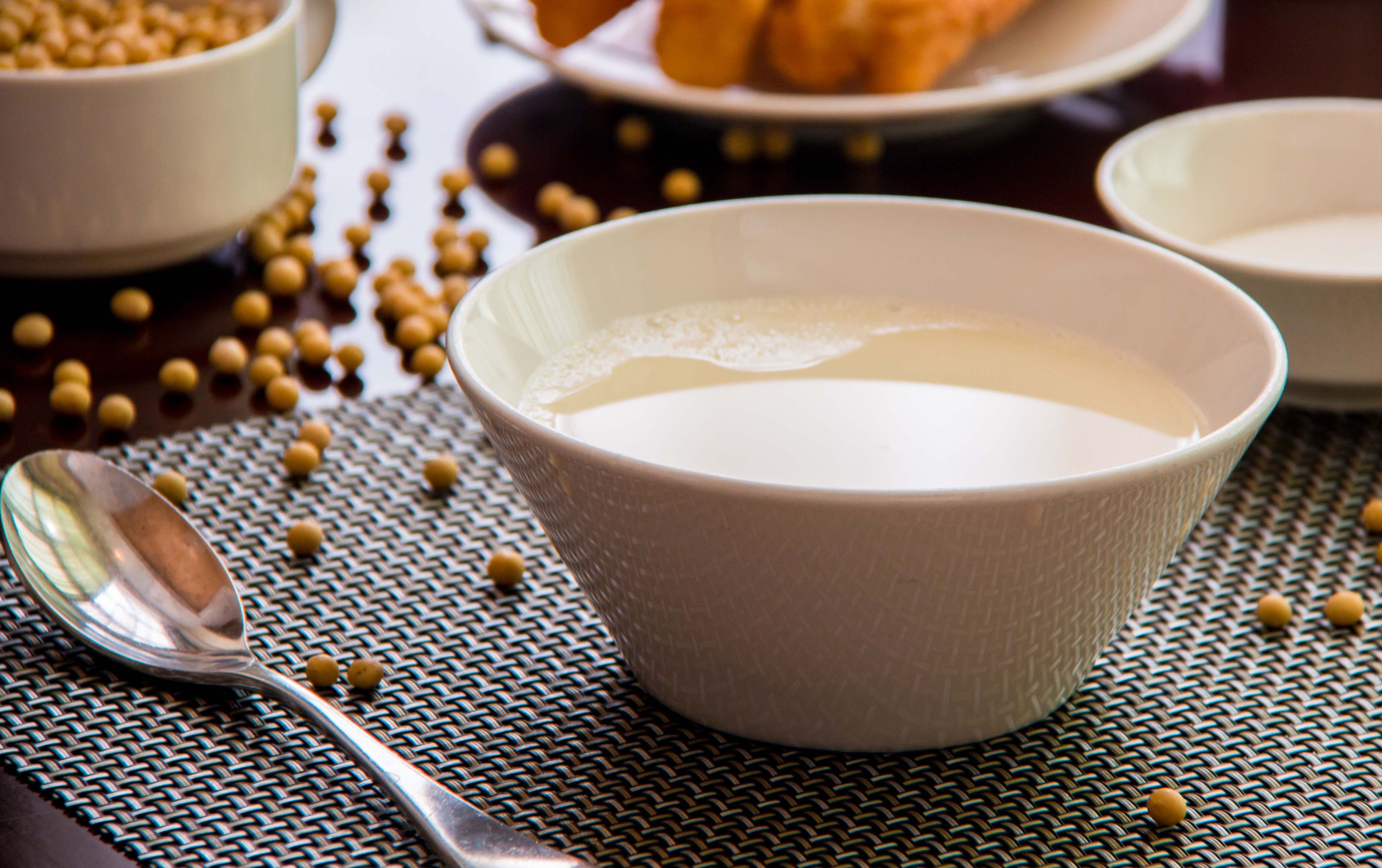 A bowl of soup with a spoon on a woven mat, surrounded by scattered beans.