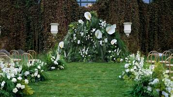 An outdoor wedding arch with white flowers and greenery, surrounded by chairs.