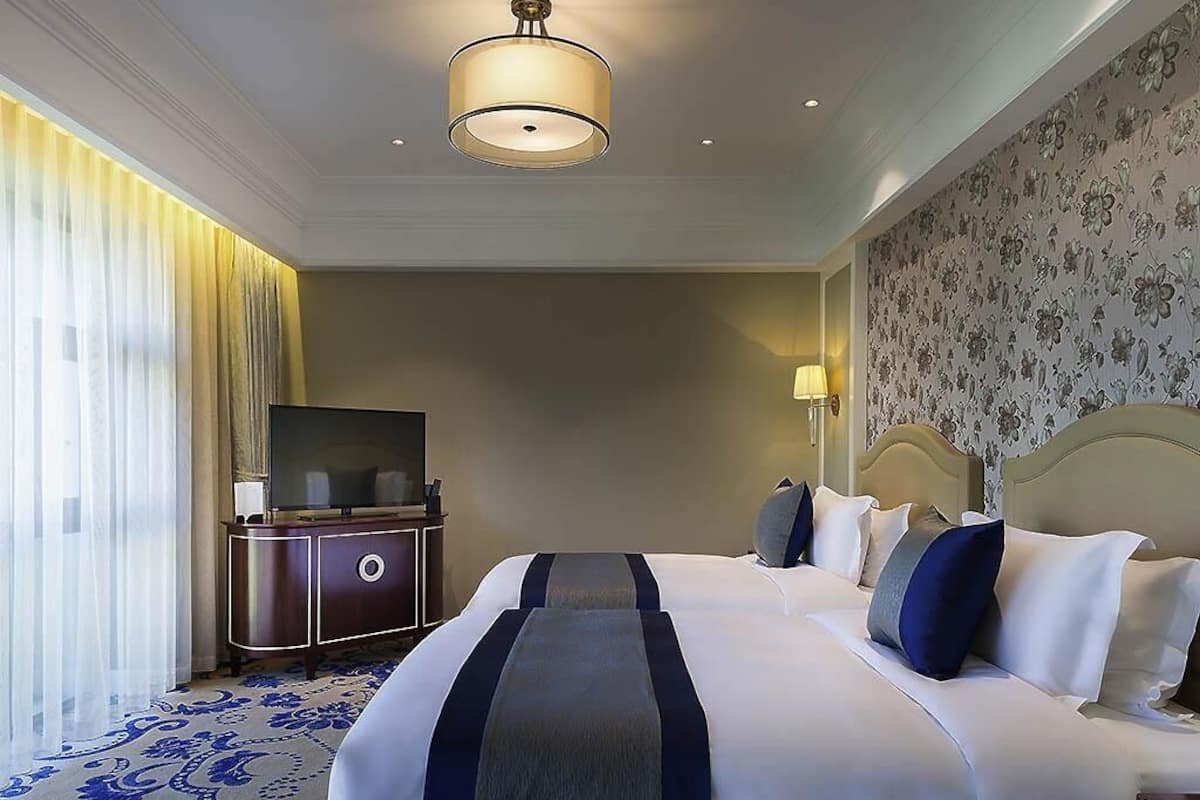 A hotel room with a large bed, a television on a wooden cabinet, a lamp, and a patterned carpet.
