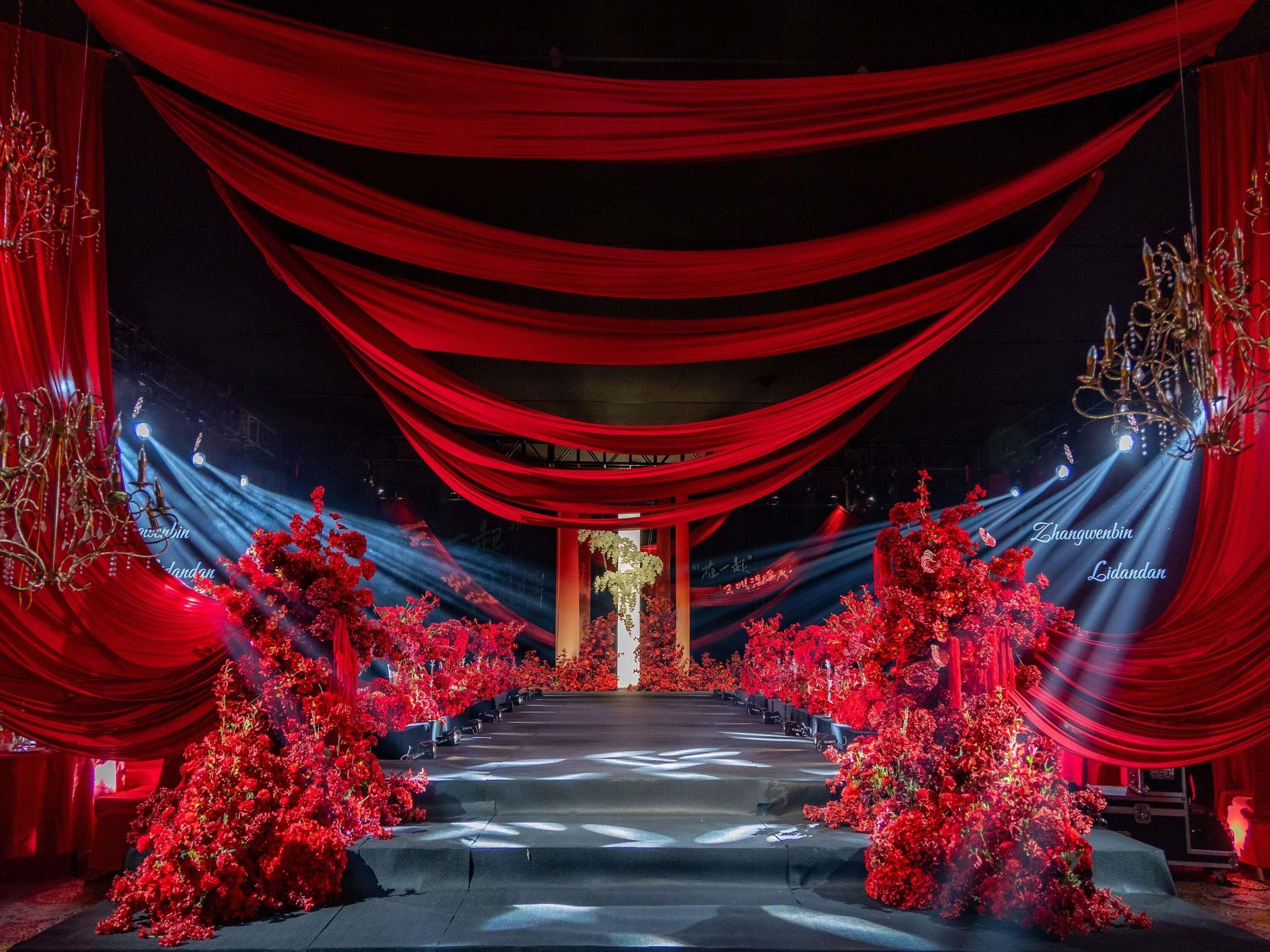 A stage with red drapes, a chandelier, and red floral arrangements.