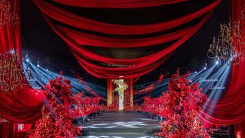 A stage with red drapes, a chandelier, and red floral arrangements.