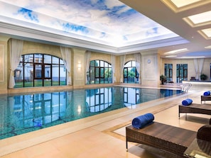 Une piscine intérieure avec des parois en verre transparent, un plafond décoré pour évoquer le ciel et un espace d’accueil doté d’un comptoir et de chaises.