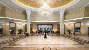 A spacious lobby with a large chandelier, marble flooring, and seating areas.