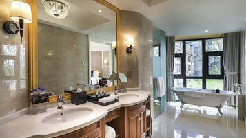 A bathroom with a double sink vanity, a freestanding bathtub, a large mirror, and a view of the outside through a window.