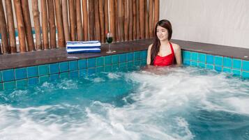 A woman in a red swimsuit in a spa pool with a wooden backdrop and a glass of green drink.