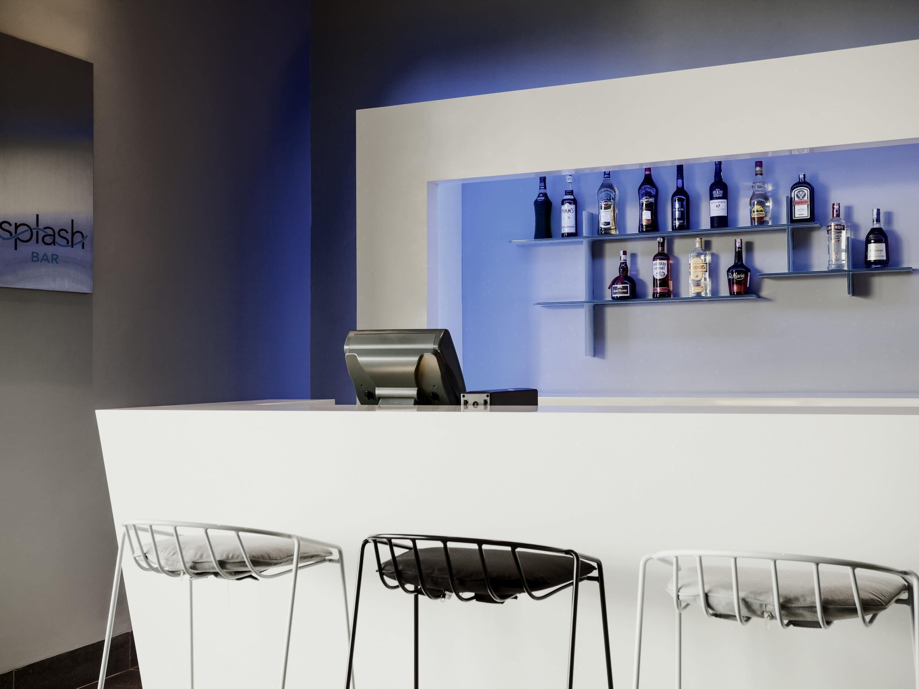 A bar area with a white counter, metal chairs, and shelves with liquor bottles.