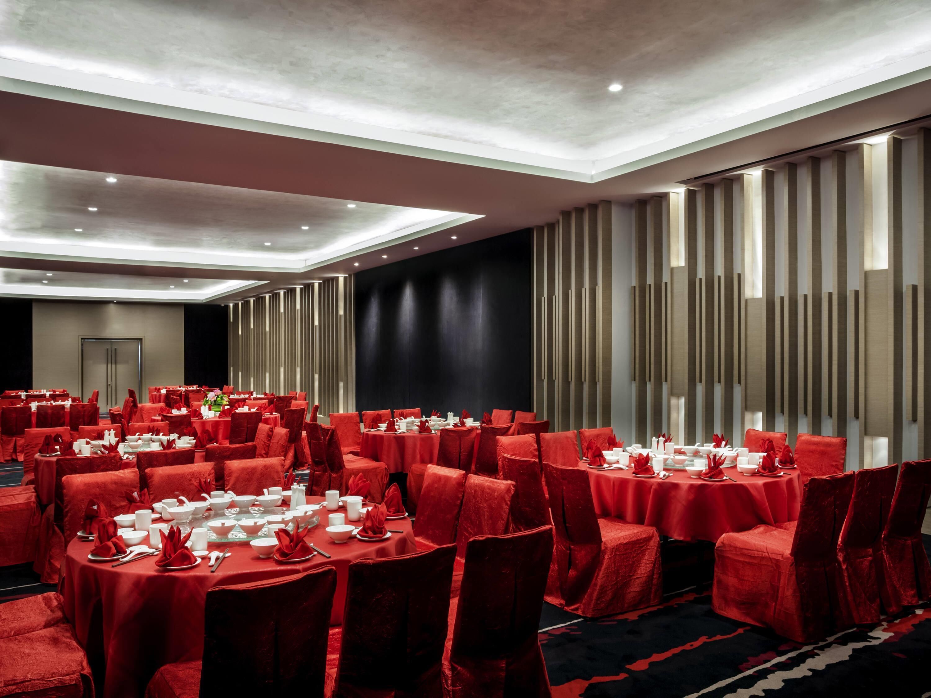 Un salón de conferencias con mesas dispuestas para un evento formal, con manteles y sillas a juego en color rojo.
