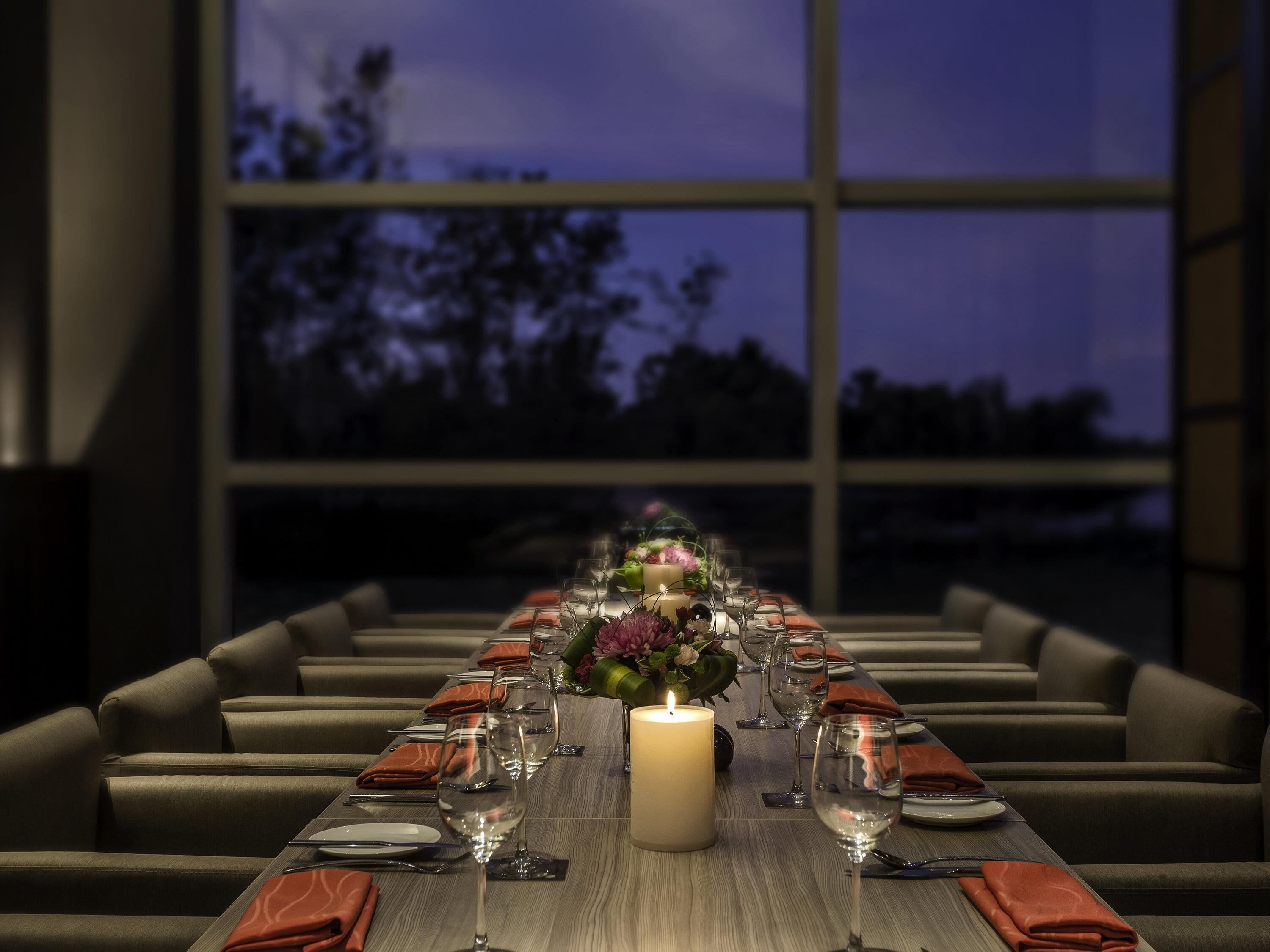 Une longue table à manger, dressée pour un repas, avec un chandelier en guise de centre de table, des verres et des serviettes pliées.