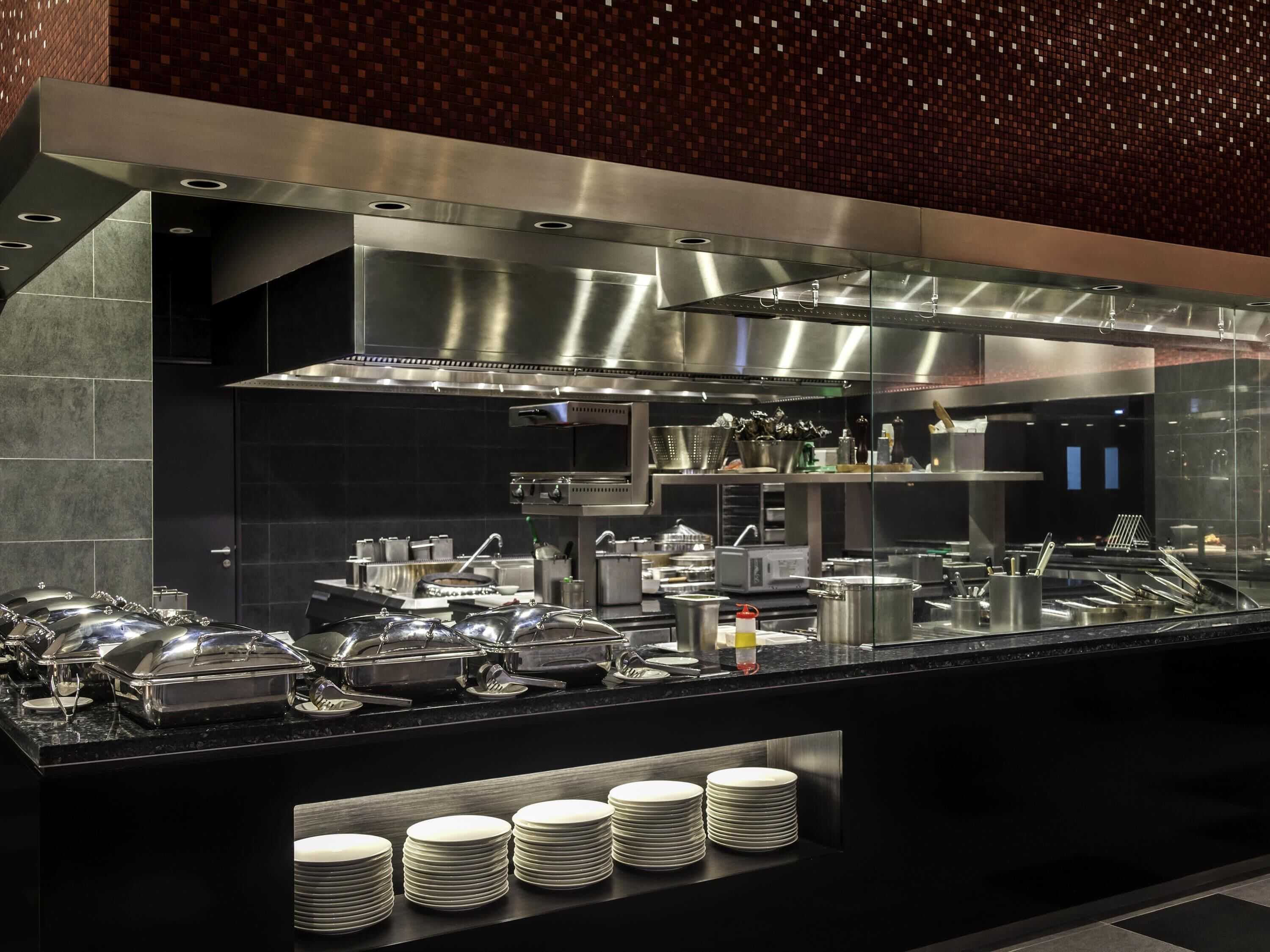 A modern kitchen with stainless steel appliances, buffet setup, and neatly stacked plates.