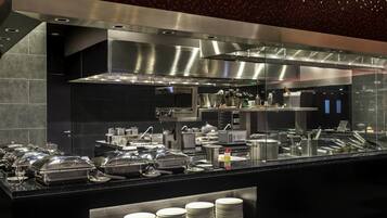 A modern kitchen with stainless steel appliances, buffet setup, and neatly stacked plates.