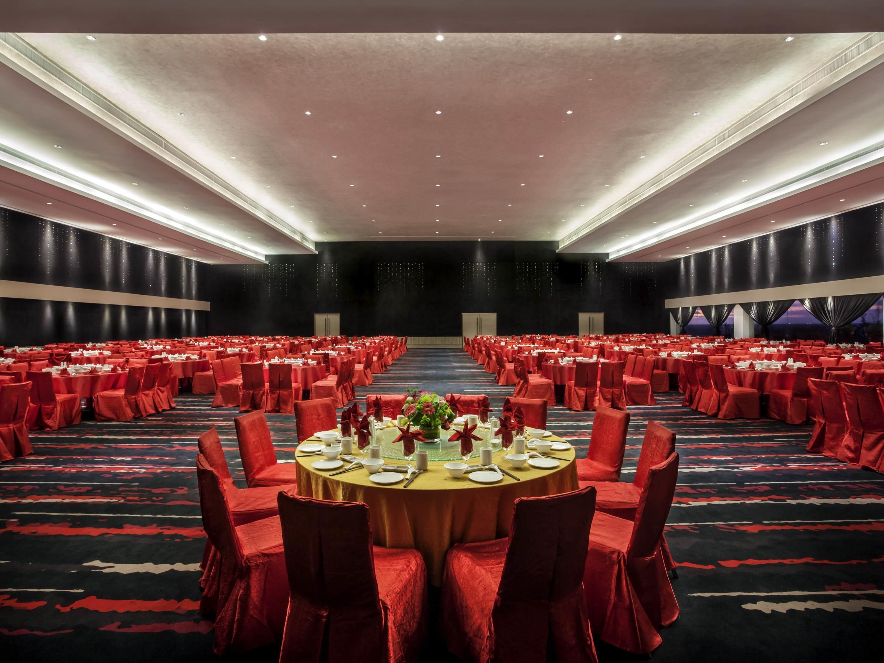 A large banquet hall with round tables, red chairs, and a carpeted floor.