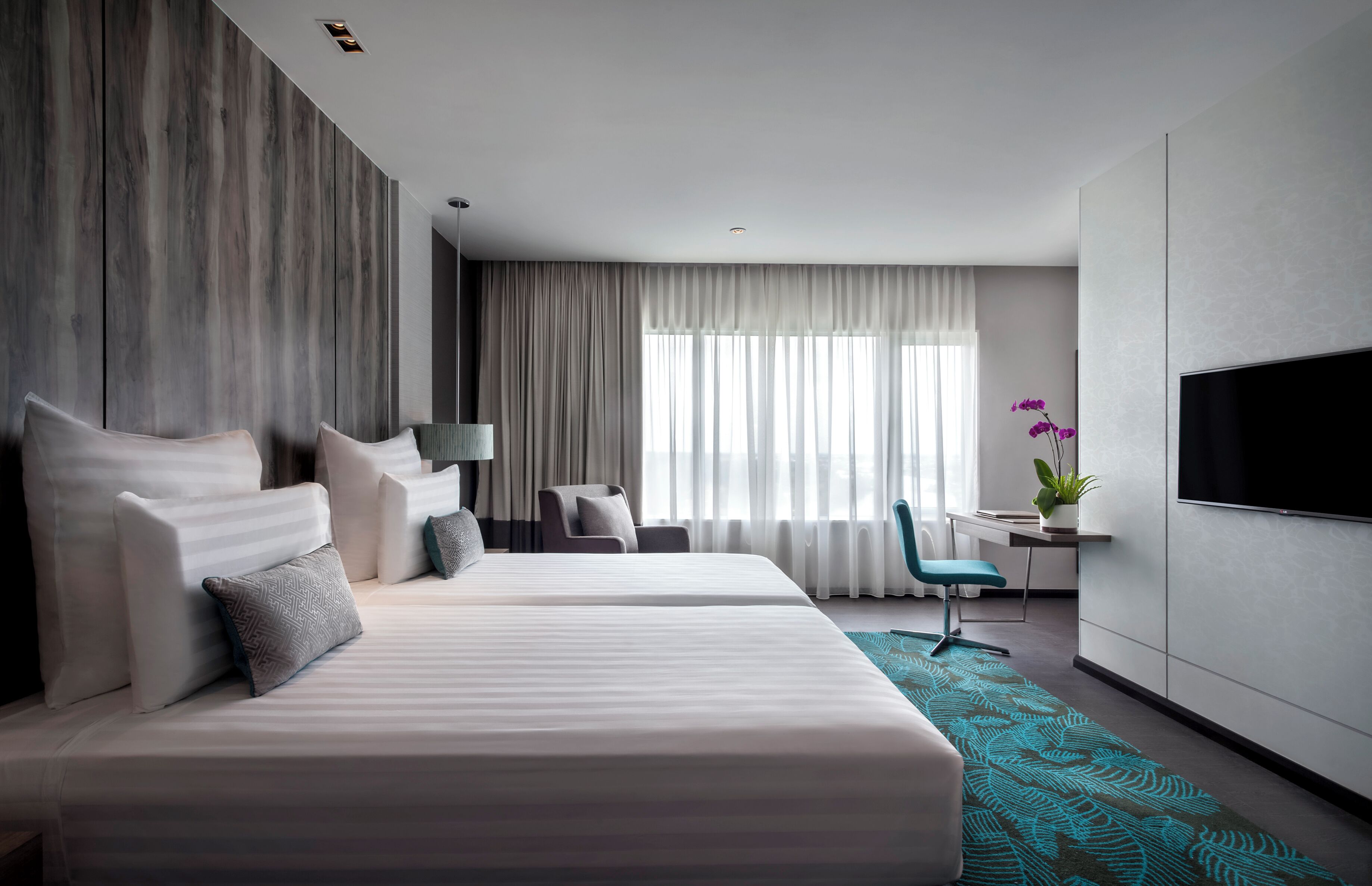 A modern hotel room with a large bed, a desk, a chair, a TV, and a window with curtains.