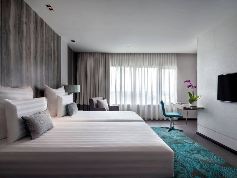 A modern hotel room with a large bed, a desk, a chair, a TV, and a window with curtains.