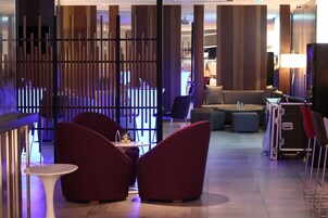 A modern hotel lobby with red seating, a bar area, and a reception desk.