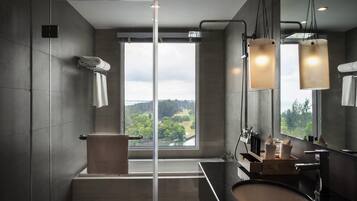 A modern bathroom with a bathtub, a large mirror, and a view of a forest through a window.