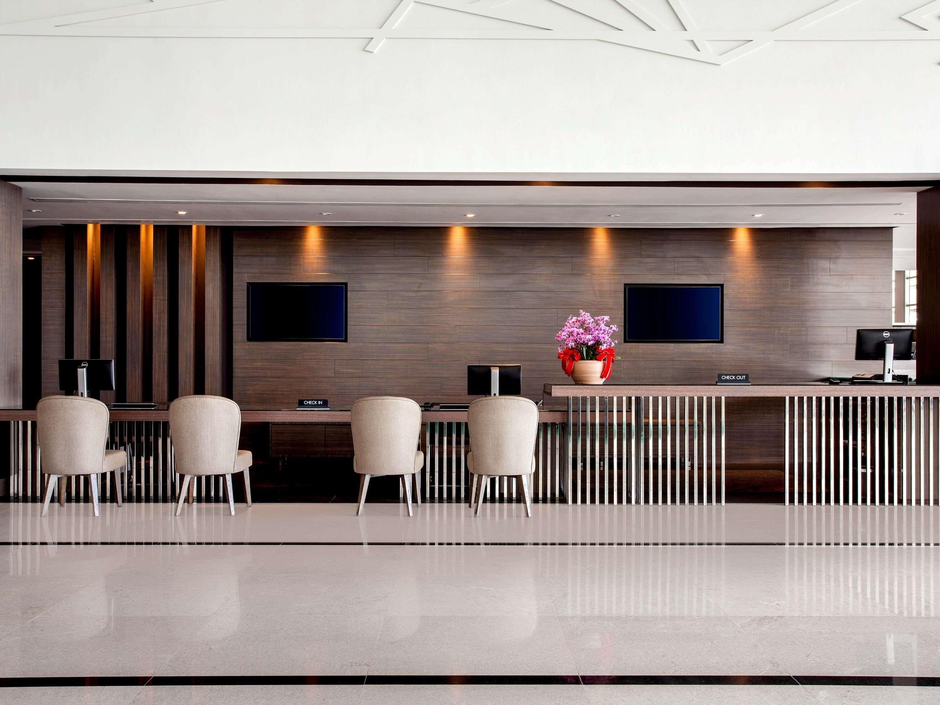 A modern reception area with a check-in counter, two flat-screen TVs, and a decorative vase with flowers.