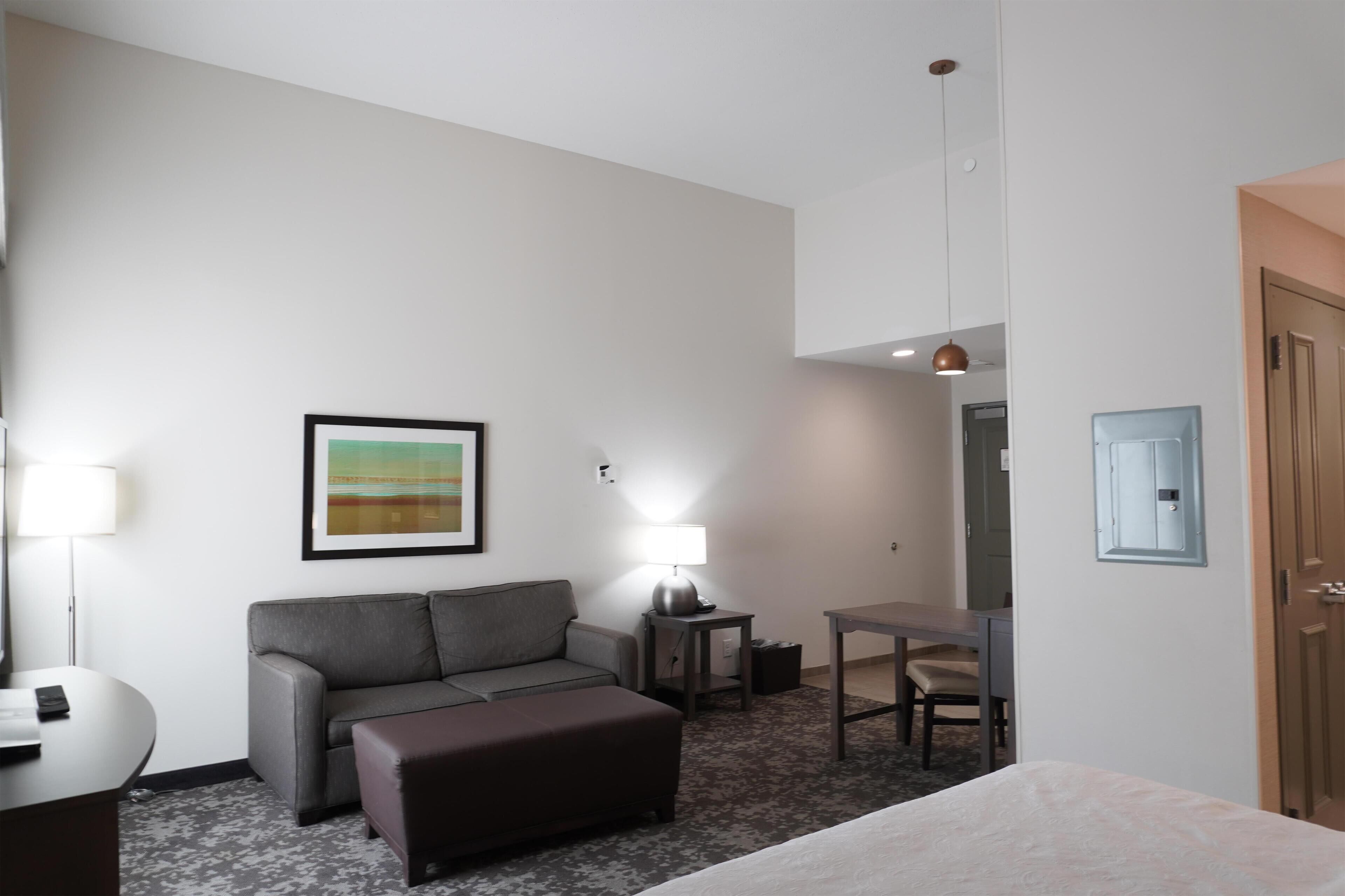 A hotel room with a sofa, a small table, a lamp, a desk, and a bed.